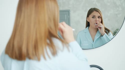 Woman Brushing Teeth in Front of Bathroom Mirror
