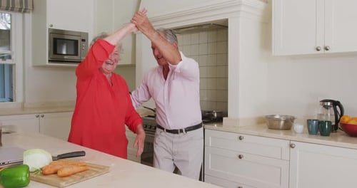 Feliz pareja mayor caucásica divirtiéndose bailando en la cocina mientras prepara la comida