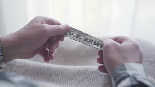 Close-up of Male Caucasian Hands Holding US Army Stripe. Lonely Veteran Recalling Memories Indoors
