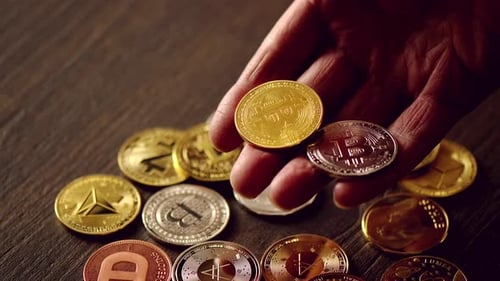 Männerhand hält Kryptomünzen und goldene Bitcoins auf einem Tisch