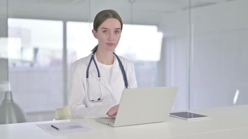 Cheerful Young Female Doctor Working on Laptop in Office