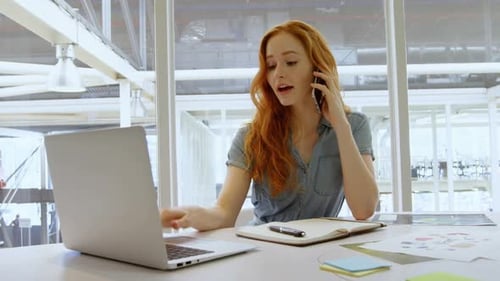 Young Woman Talking on Phone While Working on Laptop