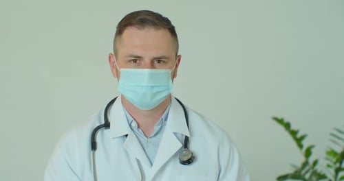 Portrait of Doctor Young Man in Glasses Wearing Mask Indoors in Hospital Looking at Camera. Medicine