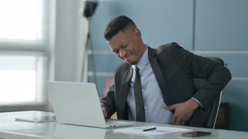 African Businessman having Back Pain while using Laptop in Office