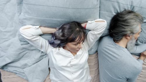 Angry Woman Looking at Sleeping Husband and Turning Away Lying in Bed Together