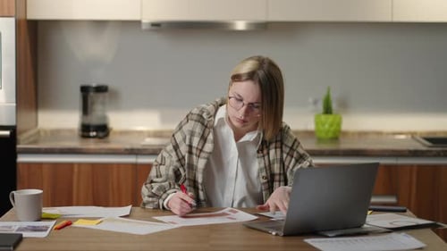A Woman with Glasses Works Remotely From Home Sitting at a Table with a Laptop and a Felttip Pen