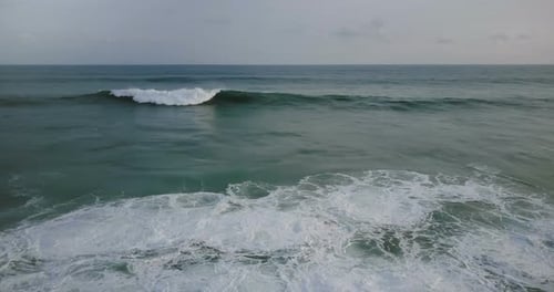Drone Flying Right Above Big Wild Blue Ocean Waves Rushing To the Shore, Foaming and Crashing Under
