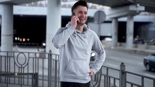 A young sports man receives a phone call outdoors near the road.