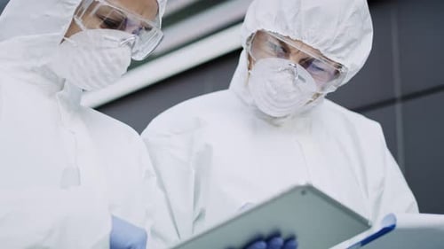 Researchers in Protective Suits Working with Tablet