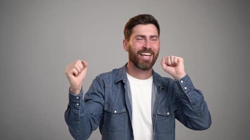 Photo of handsome young bearded man dancing isolated over grey wall background.