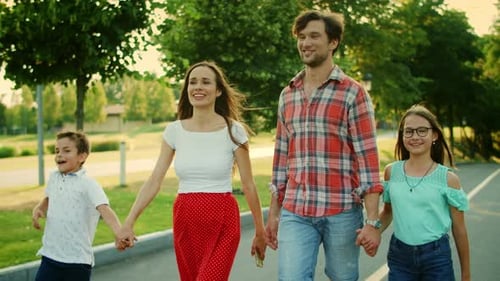 Smiling Parents and Kids Walking in Park. Joyful Family Holding Hands