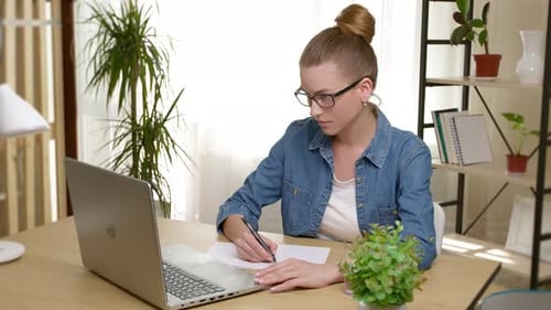 Woman Writing at Desk with Laptop