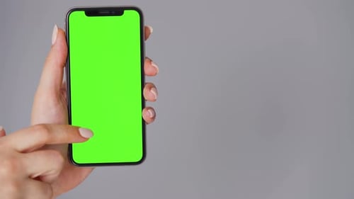 Female Hands Using a Smartphone with a Green Screen on a Gray Background. Chroma Key.