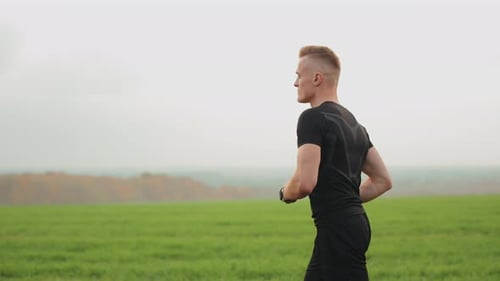 The Athlete is Running Through a Field with Green Grass