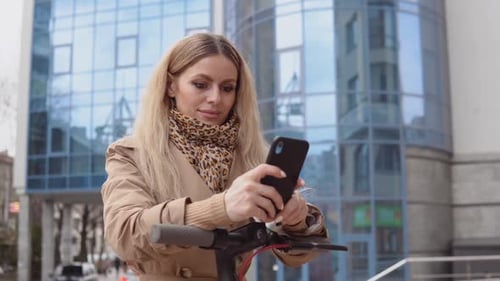Woman Using Phone with Electric Scooter in City