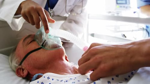 Senior Patient Receives Oxygen Mask in Hospital Bed