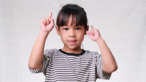 Cute little girl pointing her finger up to empty place and looking at the camera over a white studio