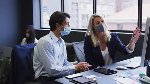 Diverse business people wearing face masks using computer in office
