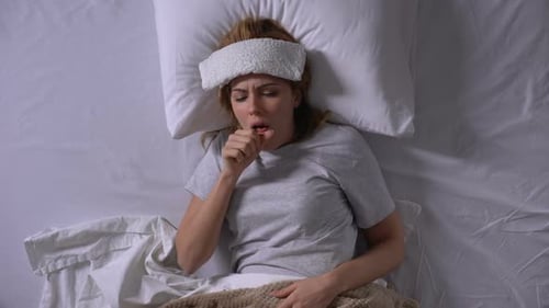Fille malade toussant, couchée dans son lit avec une compresse humide sur le front, grippe saisonnière