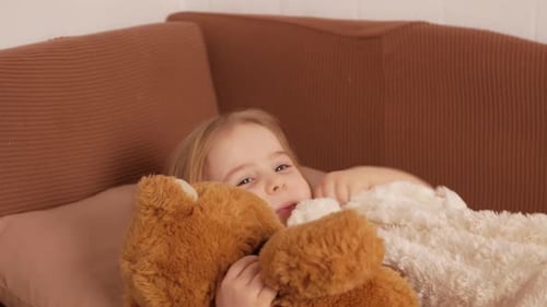 Cute Child Lying on Couch Hugging Teddy Bear