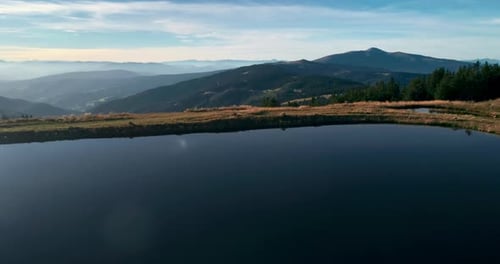 Drone Flying Above Blue Water Lake and Pine Green Forest Situated in Mountains