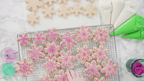 Time lapse. Flat lay. Stp by step. Icing snowflake shaped sugar cookies with pink icing.