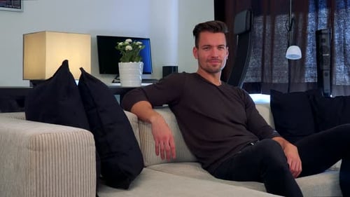 A Man Sits on a Couch, Looks at Something Off the Camera and Eventually Looks and Smiles at Camera