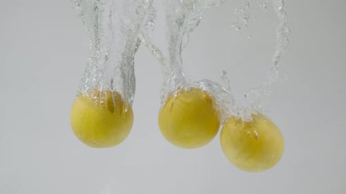 Three Yellow Fruits Dropped Into Water Creating Bubbles