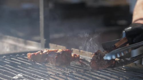 Restaurant Worker Takes Pork Rib with Silver Tongs and Cuts