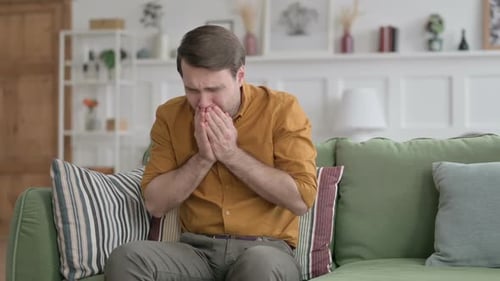 Junger Mann hustet beim Sitzen auf dem Sofa