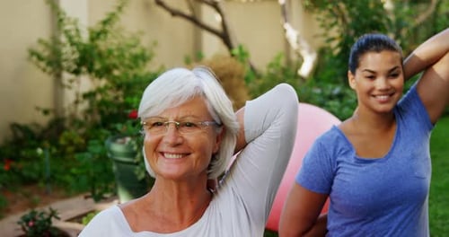 Senior woman with female trainer doing stretching exercise in garden 4k