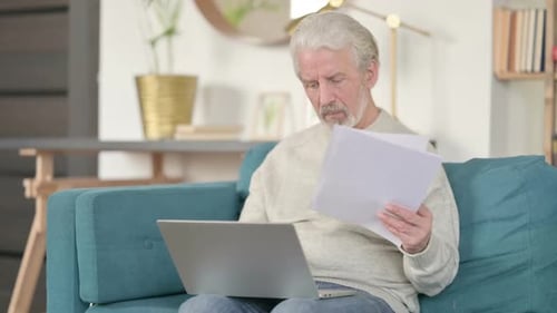 Senior Adult Reviews Documents While Working on Laptop