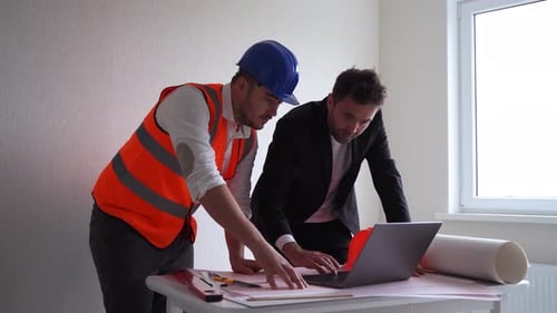 Engineers Reviewing Plans on a Laptop at Table