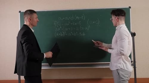 Men Discussing Equations on Chalkboard in Classroom