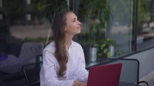 Young Positive Woman Sitting at Table with Laptop Greeting Friend Meeting in Sidewalk Cafe Outdoors