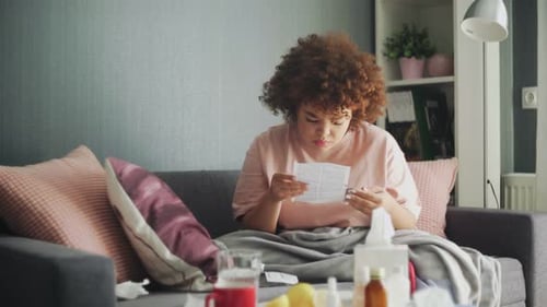 Young Woman Taking Medication on Sofa at Home