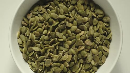 Pumpkin Seeds Falling Into A White Bowl