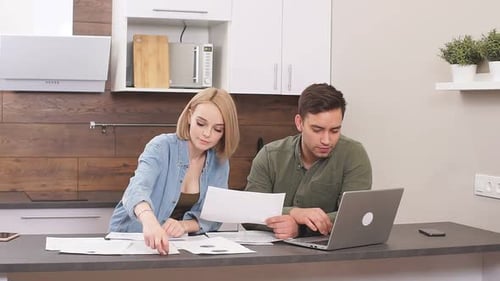 Young Couple Reviews Paperwork with Laptop in Kitchen