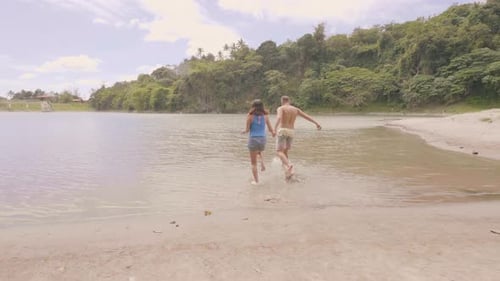 Happy Couple Holding Hands and Running in Lake Water While Summer Camping. Cheerful Man and Woman