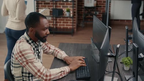 Database Programer Writing Code and Smiling While Coworker Walks By Holding Clipboard