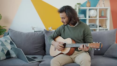 Young Adult Plays Guitar on a Couch