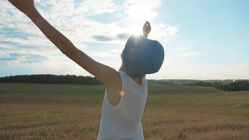 Boy in a Hat Raises Hands To the Sky in the Field
