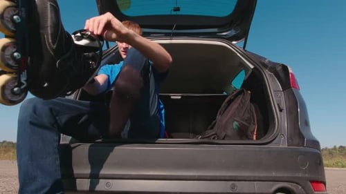 Man Laces Up Rollerblades Sitting in Car Trunk