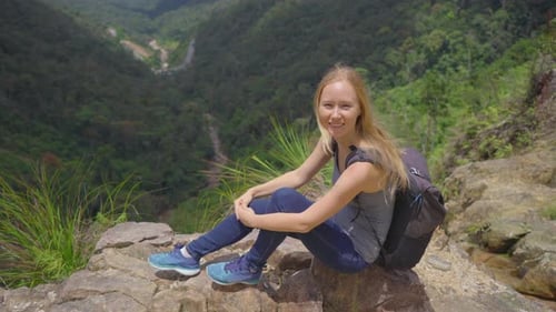 Young Woman-traveler with a Backpack in the Mountains. She Is Looking at the Majestic Valley Down