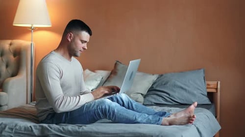 Young Adult Works on Laptop While Sitting on Bed