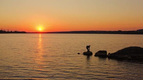River at sunset. Silhouette of a fisherman on stone.