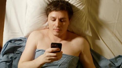 Caucasian Young Man Types By Mobile Phone In A Bed