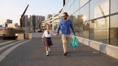 Vater mit kleiner Tochter in Uniform geht morgens zur Schule