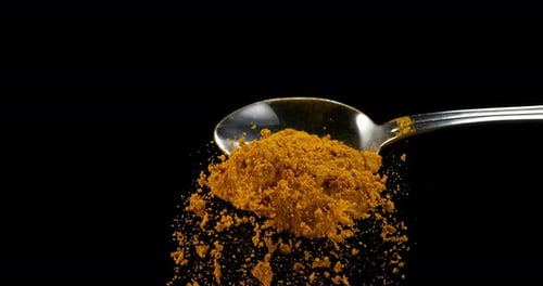 Spoon and Curry Powder falling against Black Background, Slow motion 4K