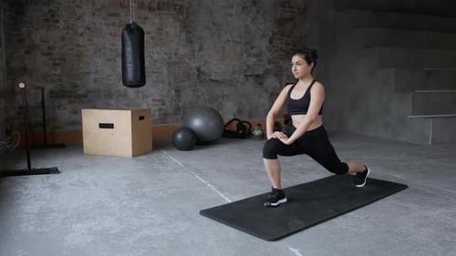 Young fit sporty brunette girl with black top, black leggings does exercises on mat in gym